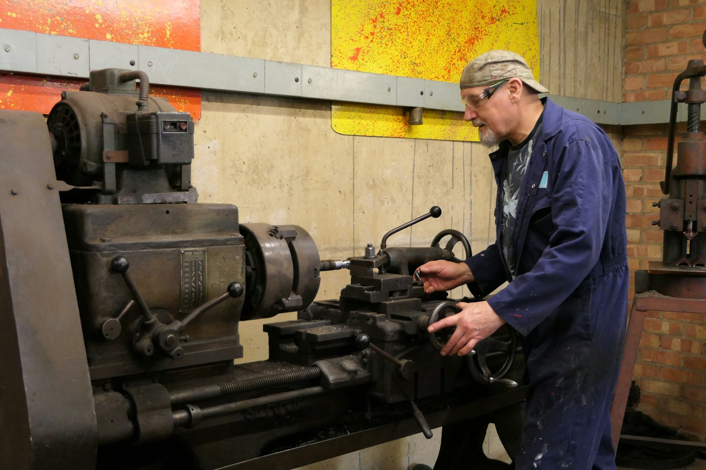 A machinist turning steel parts on an old lathe in a brick-walled shop
